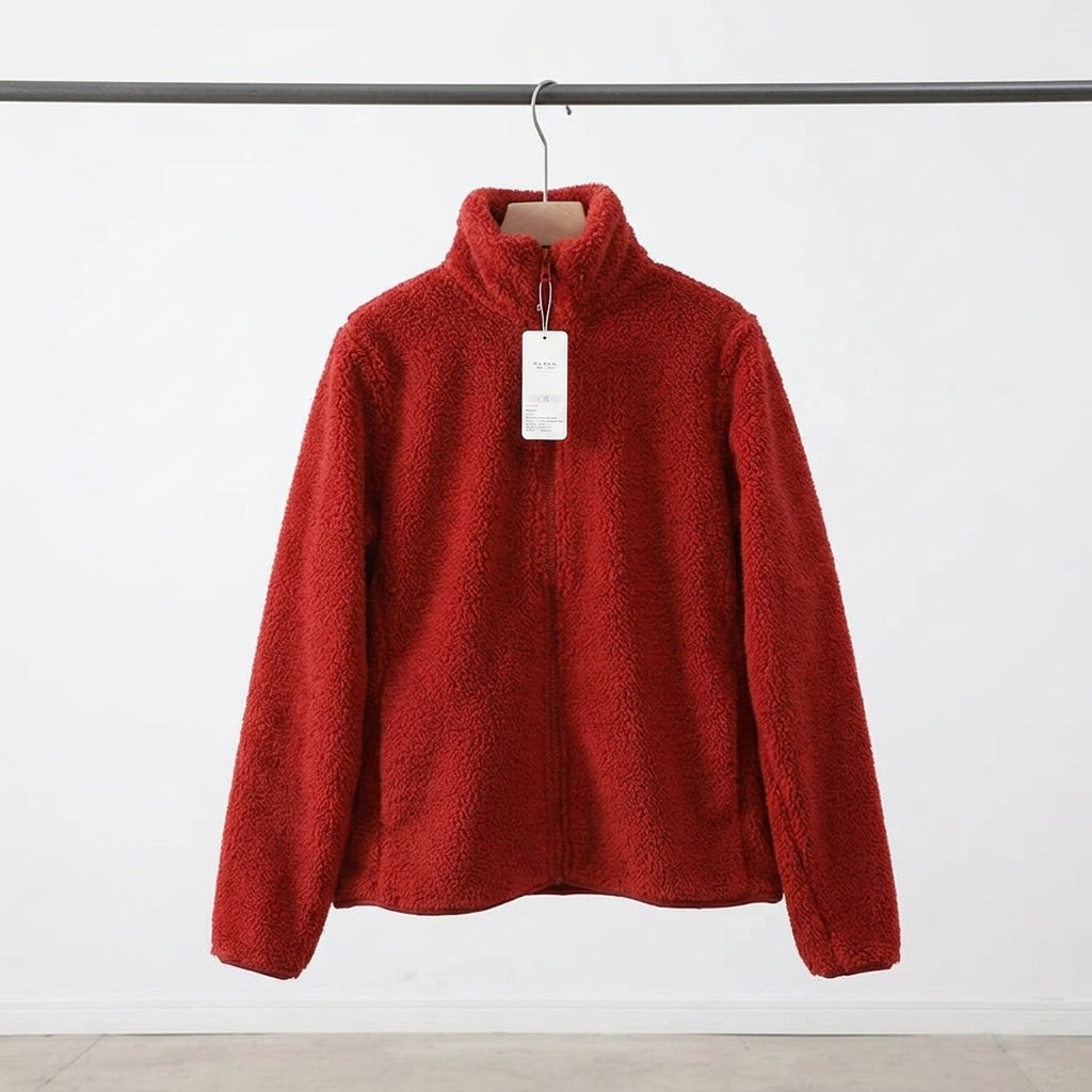 A red sherpa fleece zip-up jacket with a mock neck collar, hanging on a wooden hanger with a white tag, suspended from a dark metal rail against a white wall.