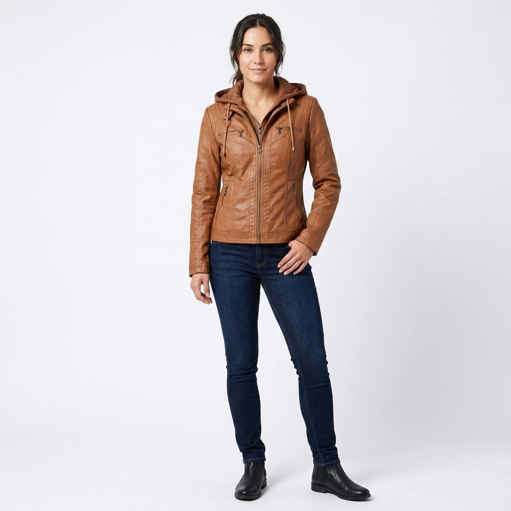 A woman modeling a brown faux-leather hooded jacket with front zipper and zip pockets, paired with dark blue skinny jeans and black ankle boots, against a light gray studio background.