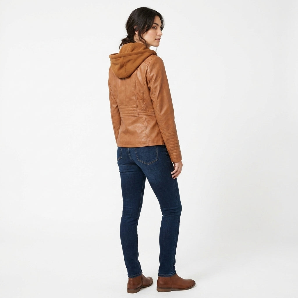 A woman shown from the back wearing a tan leather hooded jacket, dark blue skinny jeans, and brown boots, standing against a plain white studio background.