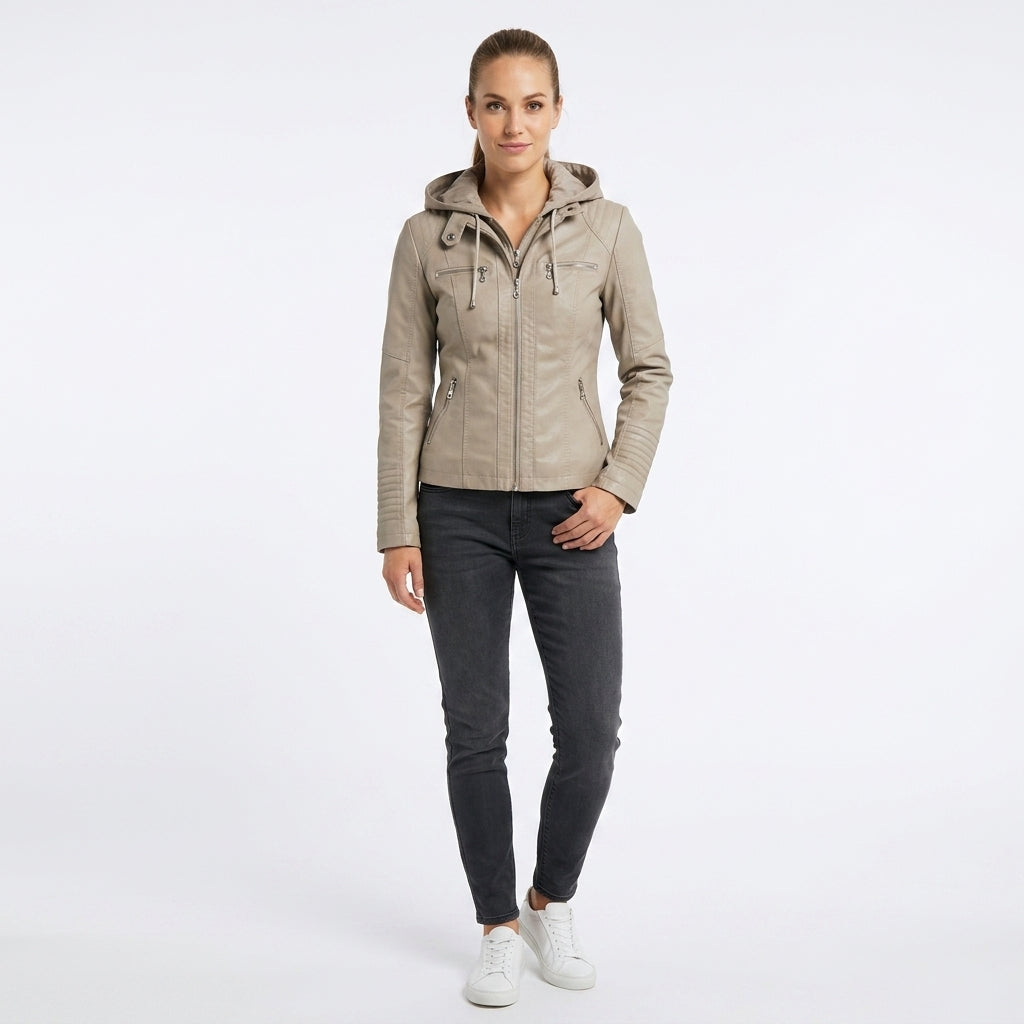 A woman modeling a light beige hooded jacket with dark gray slim-fit jeans and white sneakers, standing against a plain white studio background.