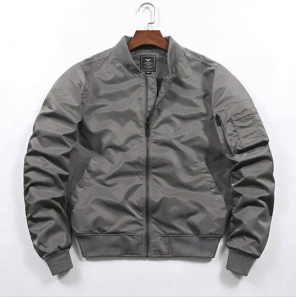 A gray nylon bomber jacket hanging on a wooden hanger against a plain white background.