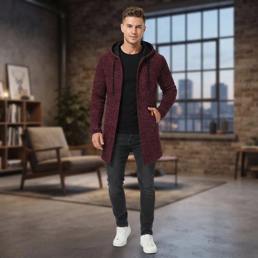 A man modeling a maroon hooded knit cardigan over a black t-shirt, dark gray jeans, and white sneakers in a modern loft-style room with brick walls and a large window.