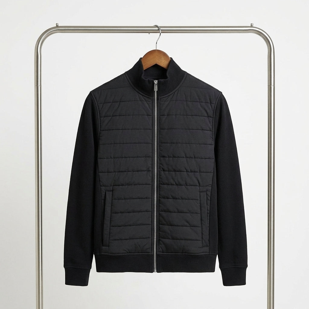 A black zip-up jacket with a quilted chest panel and solid sleeves, hanging on a wooden hanger from a metal clothing rack against a plain white background.