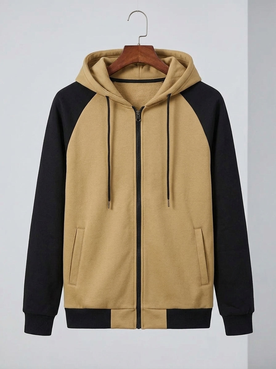 A color-blocked zip-up hoodie with a tan body and black sleeves, hanging on a wooden hanger against a light gray background.
