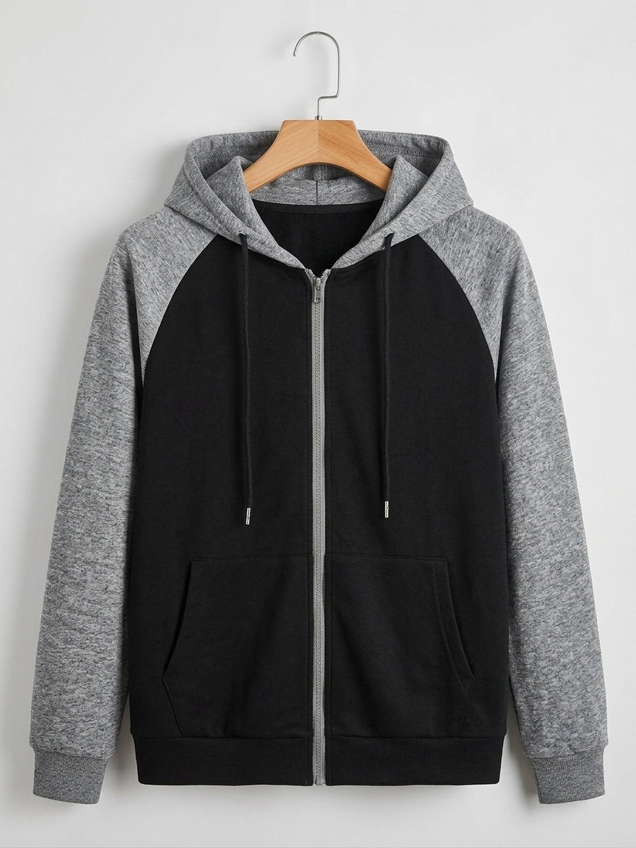 A colorblock zip-up hoodie with a black body and heather gray raglan sleeves and hood, hanging on a wooden hanger against a light gray wall.