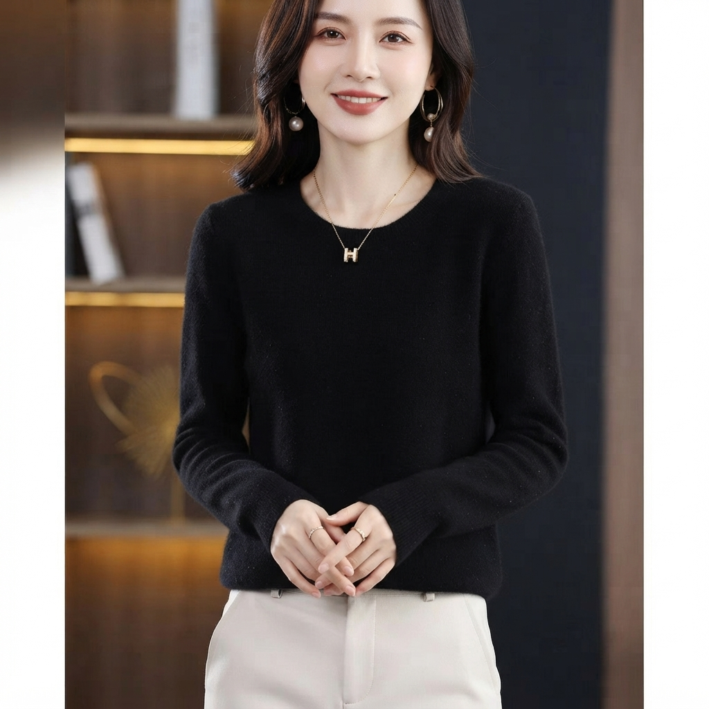 A woman wearing a black long-sleeve crewneck knit sweater and light beige trousers, standing in an indoor setting with a blurred background.