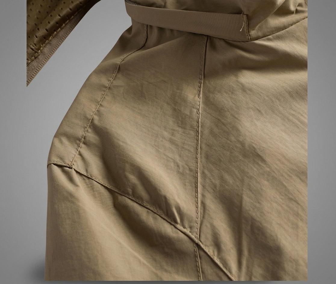Close-up of a beige or khaki fabric garment, showing the texture, stitching, and part of a belt or strap at the top against a neutral gray background.