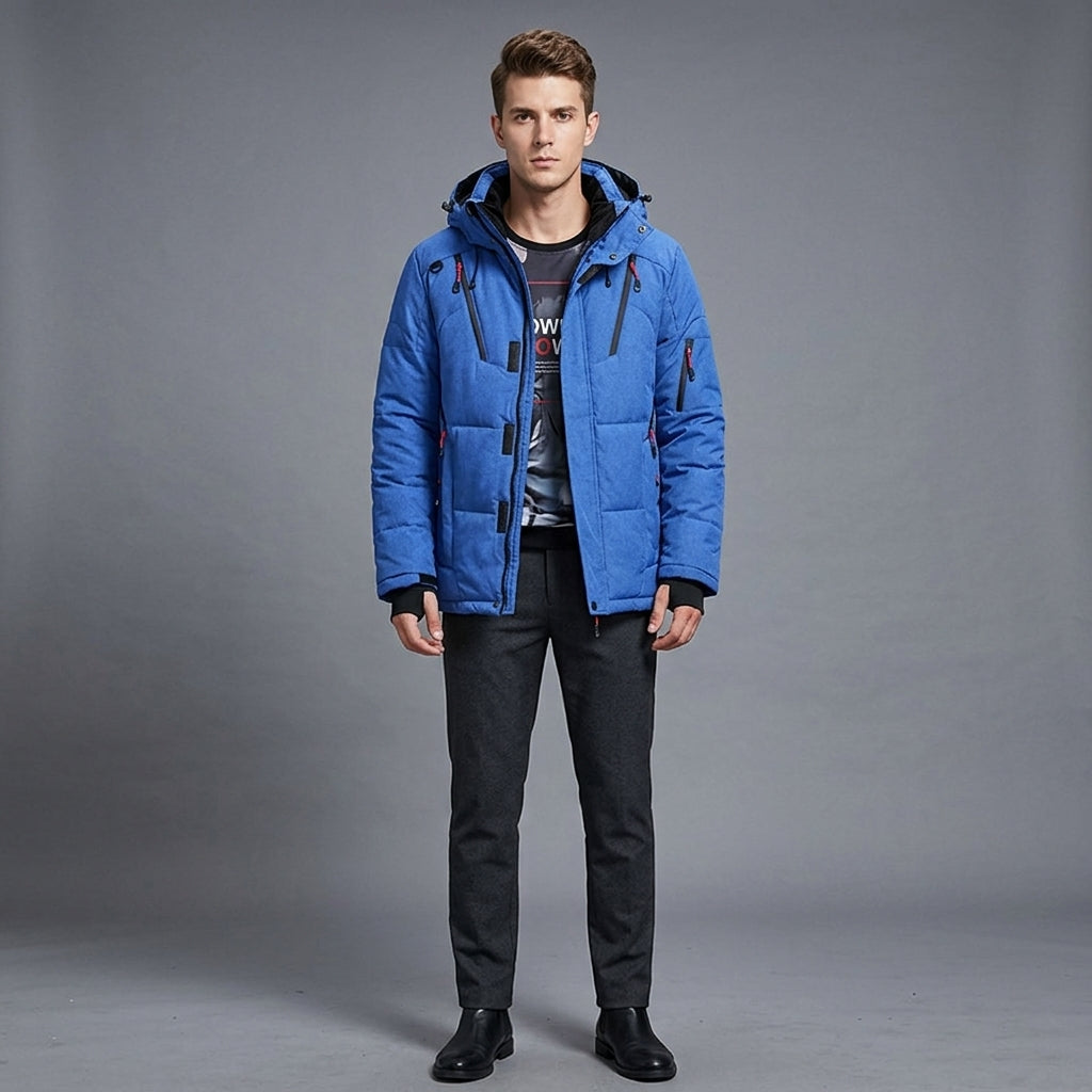 A man modeling a bright blue hooded puffer jacket over a dark graphic t-shirt, black pants, and black boots, standing against a neutral gray studio background.