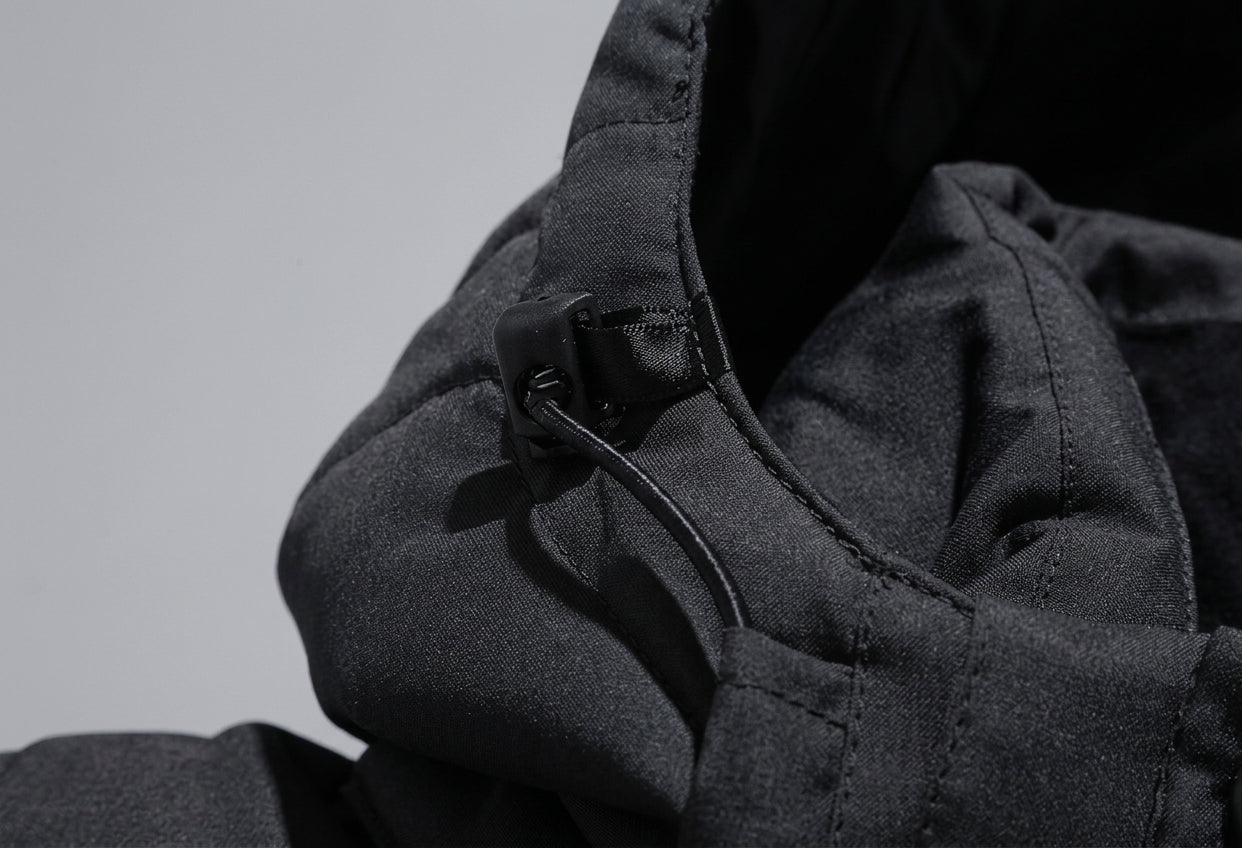 Close-up detail of a dark gray hooded jacket with a black drawstring and toggle closure, set against a neutral light gray background.