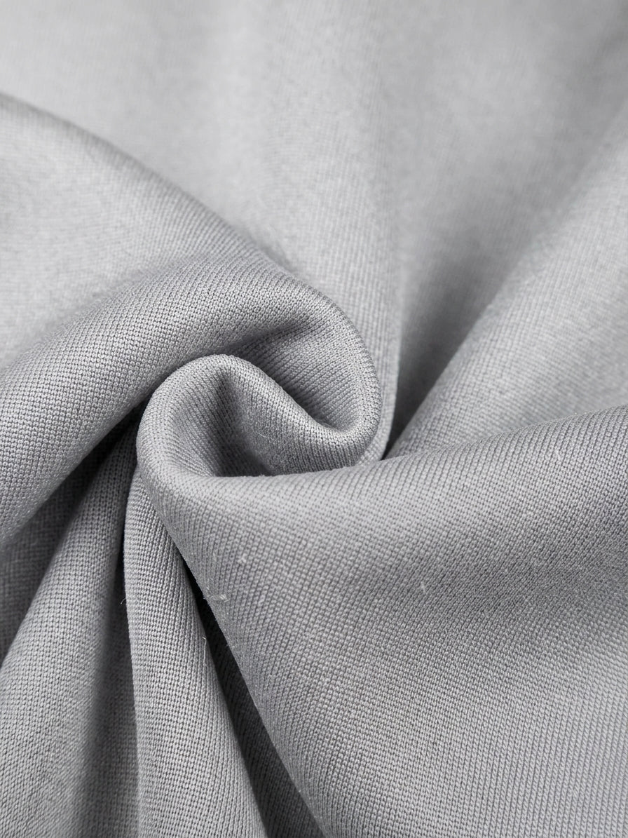A close-up of light gray fabric with soft folds and a textured woven surface.