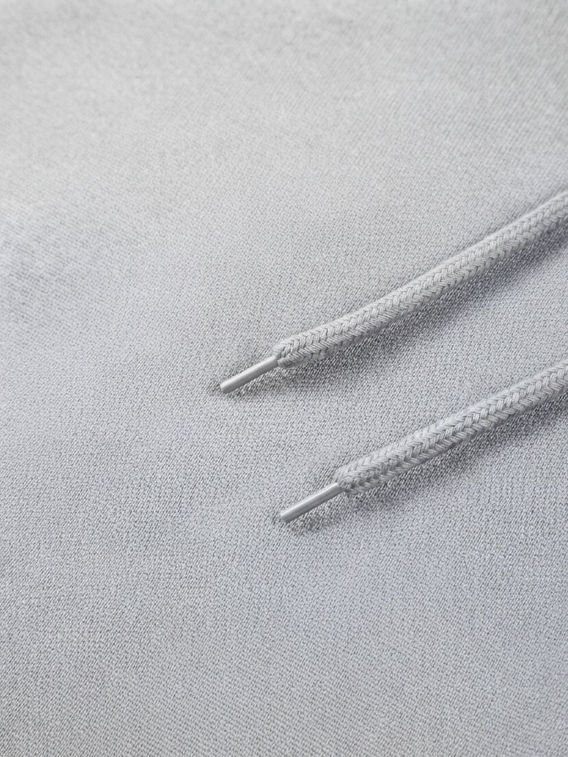 Close-up of a light gray textured fabric with two matching drawstrings and silver metal tips.