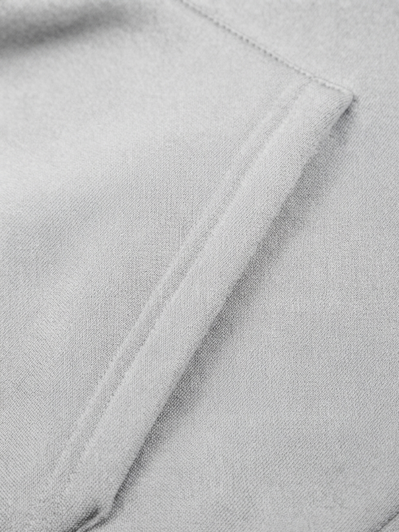 Close-up of a light gray fabric surface with a stitched pocket or fold detail.