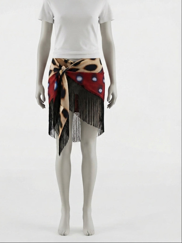 A mannequin wearing a white short-sleeve T-shirt and a patterned wrap skirt with black fringe. The skirt features a red base with leopard print, black spots, and white polka dots.