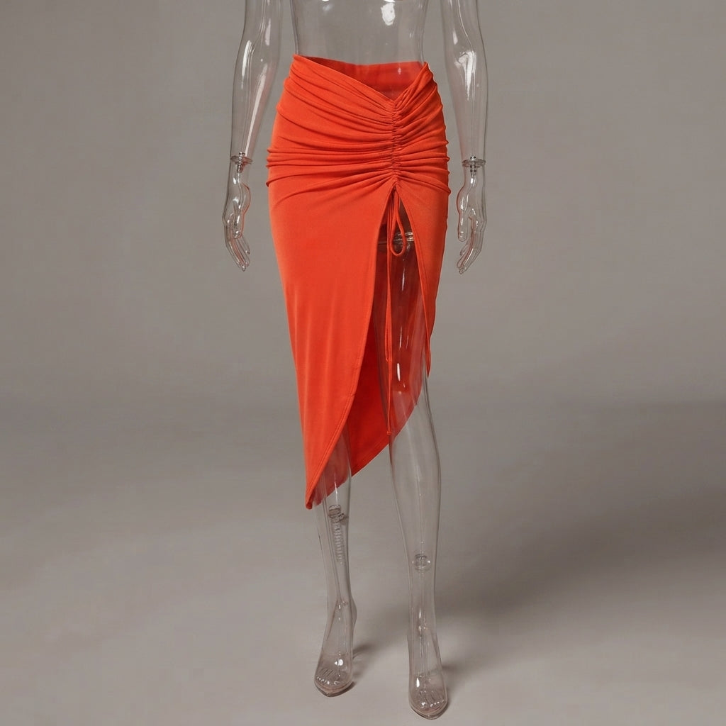 Bright orange asymmetrical ruched wrap skirt displayed on a clear acrylic mannequin against a neutral gray studio background.
