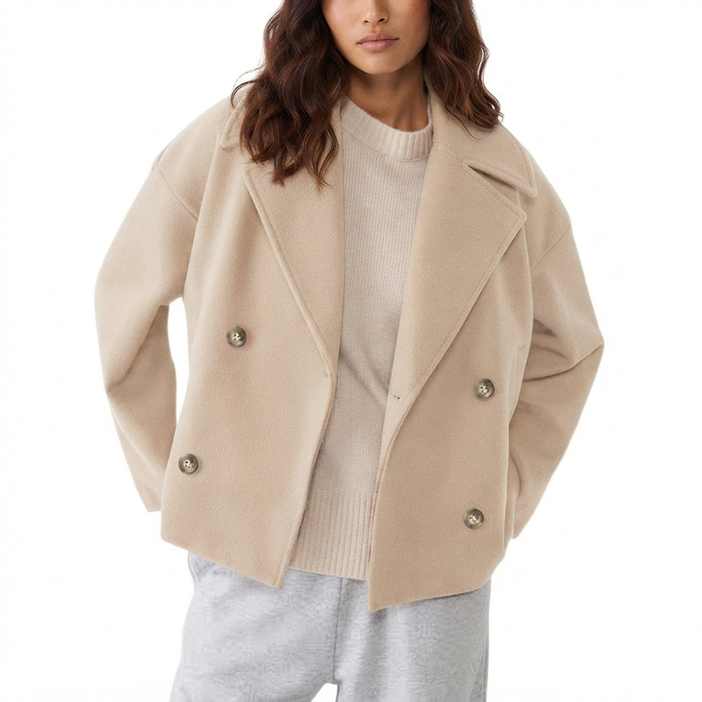 A woman wearing a beige double-breasted wool-blend coat over a cream ribbed sweater and light gray sweatpants, shown from the chest down against a plain white background.