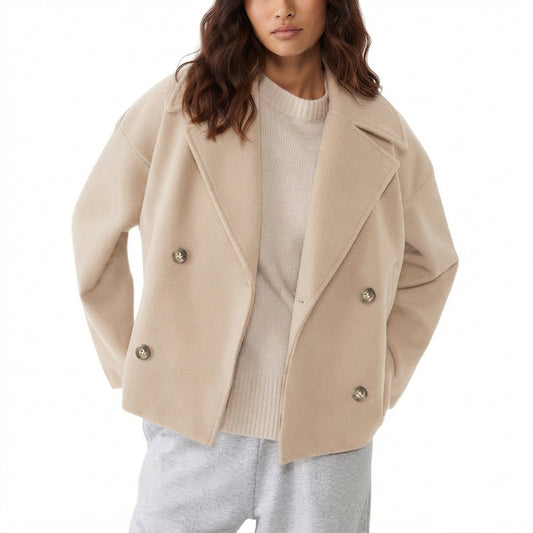 A woman wearing a beige double-breasted wool-blend coat over a cream ribbed sweater and light gray sweatpants, shown from the chest down against a plain white background.